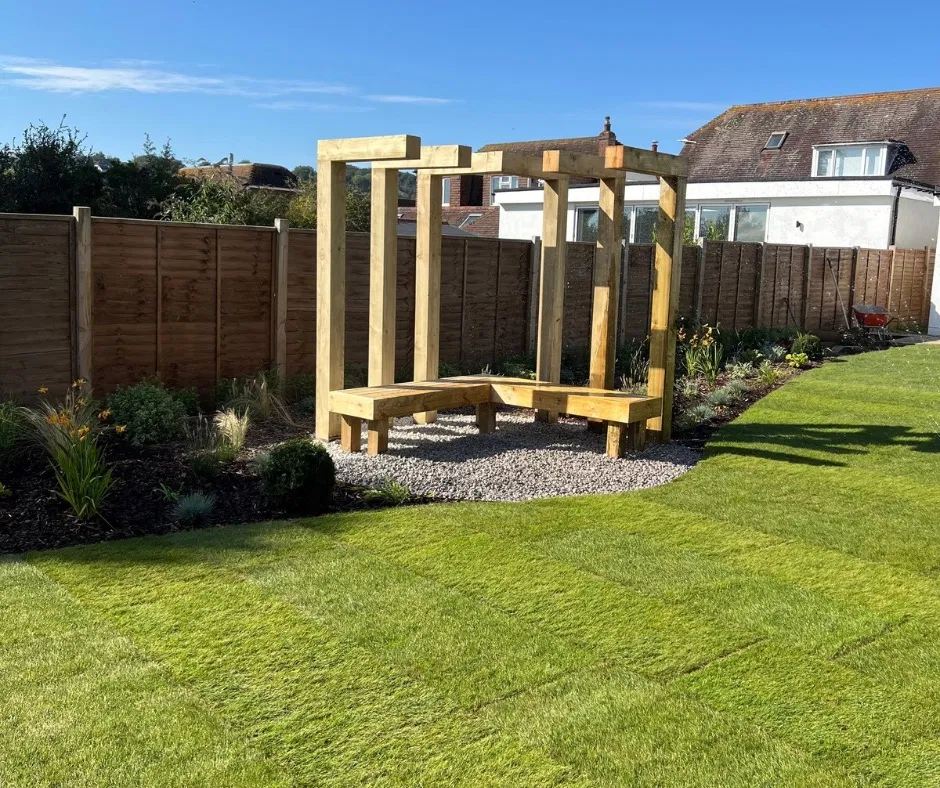 A fire pit area with gravel and wooden bench and structure for climbing plants in a garden in Findon Valley